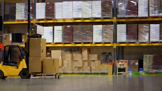 dit is binnen een groot magazijn van een warehouse met veel dozen en producten voor fulfillment met een heftruck die een pellet met dozen vast heeft